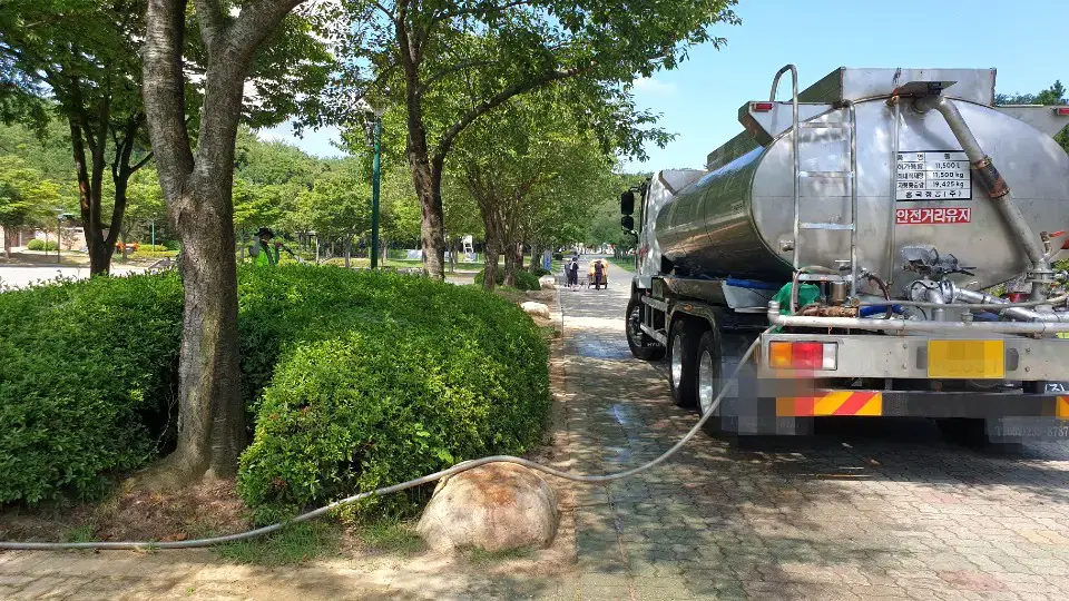 공원 산책로 옆에 세운 급수차에서 호스를 빼 나무와 관목에 물을 주는 모습