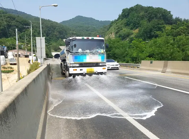 산 아래 국도에서 살수차가 차로 폭 전체에 물을 뿌리며 도로를 씻어 내는 모습